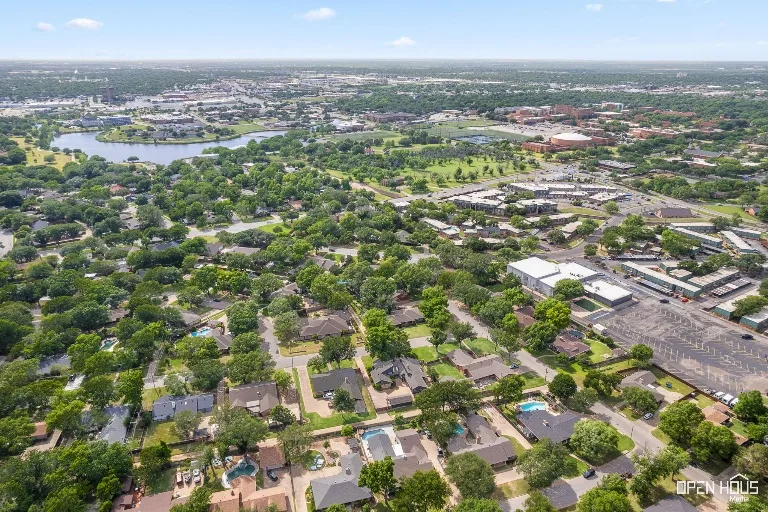 An aerial drone view of a Wichita Falls neighborhood, showing lush green spaces and suburban residential blocks.