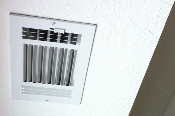 Technician cleaning an HVAC vent with a vacuum hose