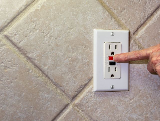 A close-up of a GFCI outlet with its test and reset buttons on a white wall