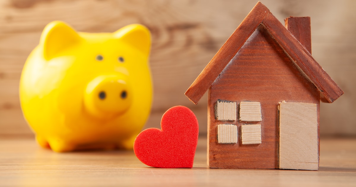 Yellow piggy bank with wooden house and red heart