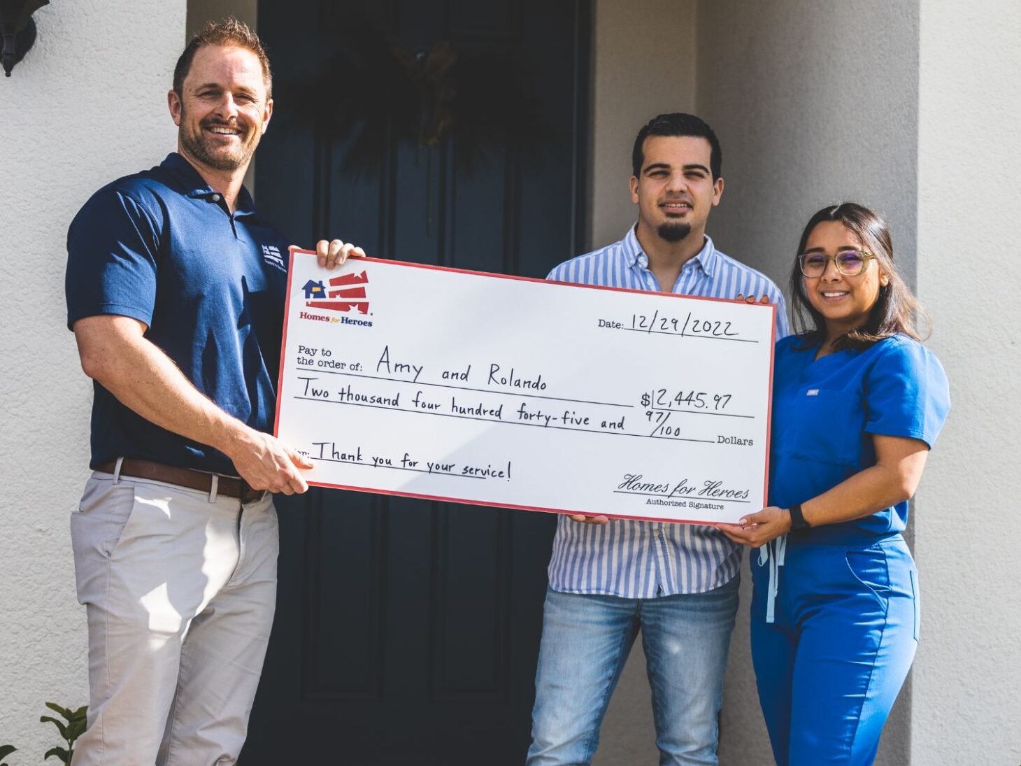 a veteran and spouse holding a large Homes for Heroes savings check in front of their new home