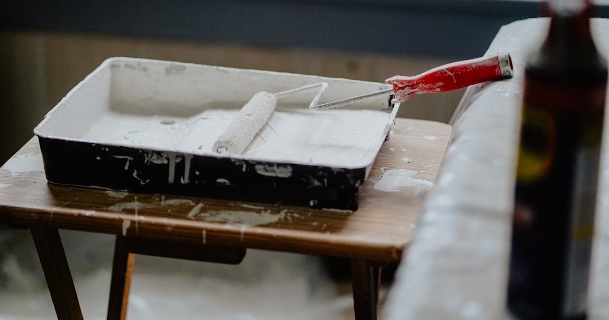 A paint roller with a red handle in a tray of white paint