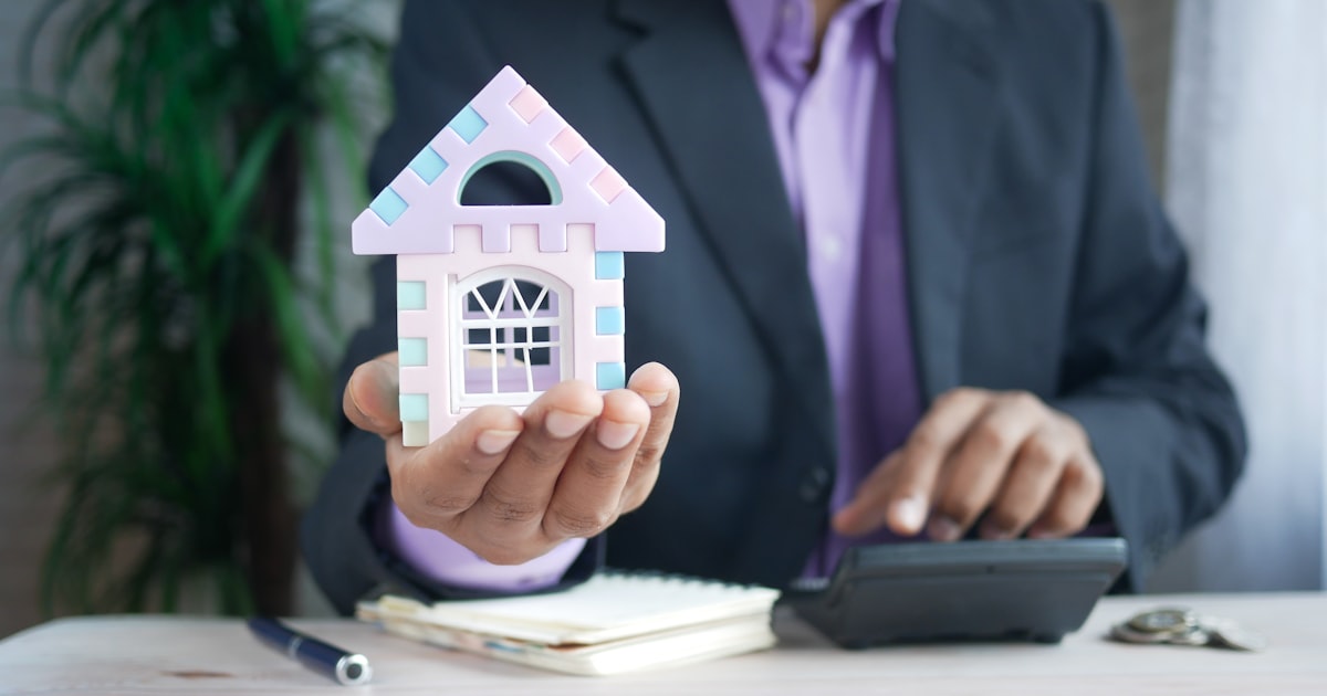 man holding model house at desk with calculator