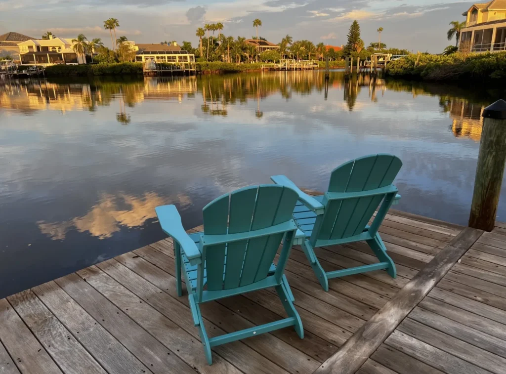 Two teal Adirondack chairs on the Calvert family's dock overlooking a calm Apollo Beach, FL canal at sunset