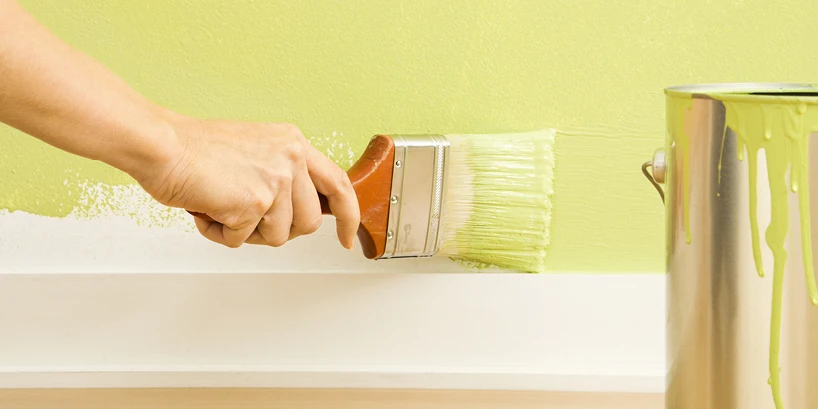 A professional painter demonstrates the precision required for "cutting in" at the ceiling line using high-end interior paint.